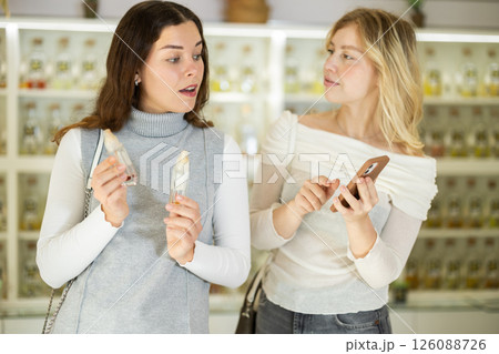 Girl shows phone screen to her female friend in perfume store 126088726