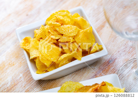 Crispy potato chips in white square ceramic plate on wooden table 126088812