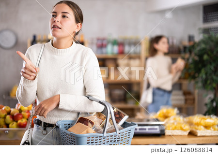 Portrait of girl shopper with a shopping cart choosing some products in supermarket 126088814
