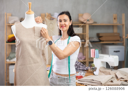 Woman tailor connects parts of dress on mannequin 126088906