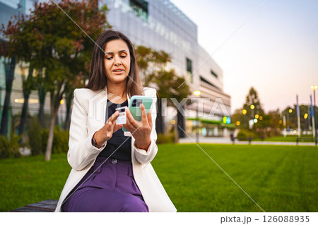 Businesswoman online shopping on a mobile phone at the park after work 126088935