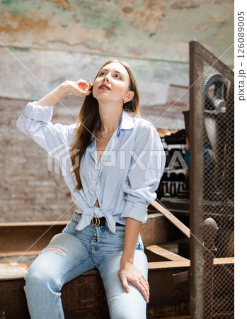 Young woman in jeans and tied shirt posing in destroyed plant Young woman in jeans and tied shirt posing in destroyed plant 126089005