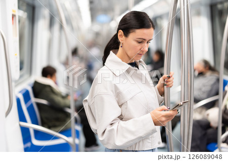Woman stand in metro carriage, scrolls through social media feed 126089048