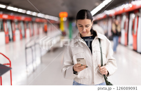 Girl is standing on metro platform station, scrolling through mobile phone 126089091