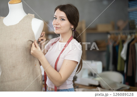 Female tailor sews new dress on a mannequin in sewing studio 126089128