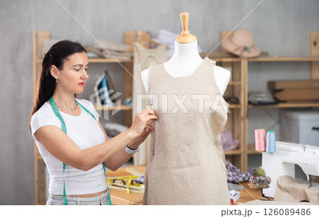 Woman tailor connects parts of dress on mannequin Woman tailor connects parts of dress on mannequin 126089486