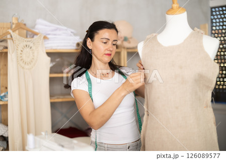 Woman tailor connects parts of dress on mannequin 126089577