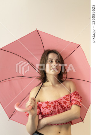 woman in a pink blouse with open shoulders holding a large pink umbrella 126089628