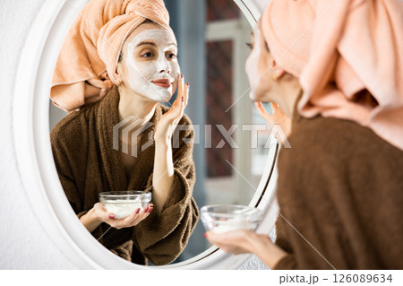 Woman smoothing face cream in front of mirror 126089634