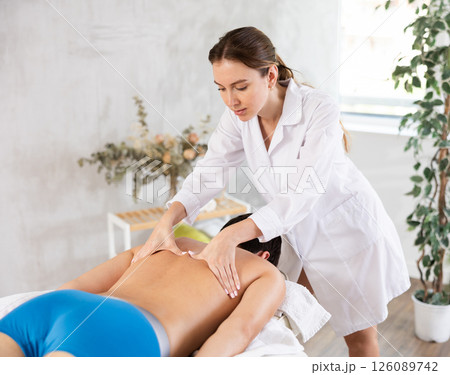 Professional young masseuse performing back massage for male patient 126089742