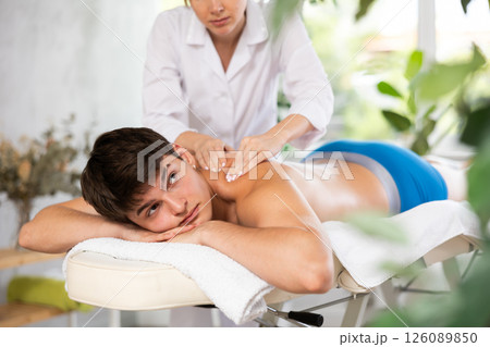 Cropped circumcised young woman performs back shoulder massage to male client. Cropped circumcised young woman performs back shoulder massage to male client. 126089850