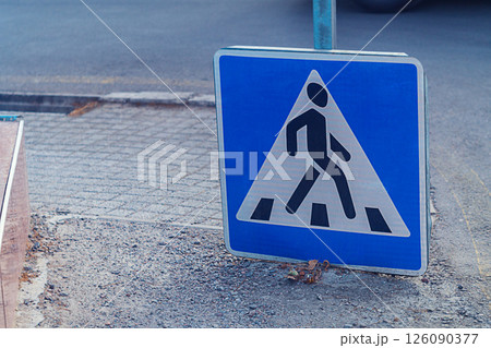 A road sign indicating a place for a pedestrian crossing slid down onto the sidewalk. The symbolism of a visual representation of how pedestrians should cross the road A road sign indicating a place for a pedestrian crossing slid down onto the sidewalk. The symbolism of a visual representation of how pedestrians should cross the road 126090377