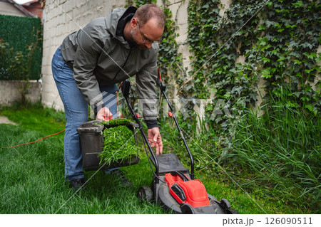 Man carefully trims grass in a lush garden as evening sunlight filters through green leaves Man carefully trims grass in a lush garden as evening sunlight filters through green leaves 126090511
