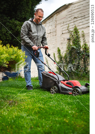 Lawn care enthusiast practices weekend gardening with electric mower in a well-kept yard 126090513