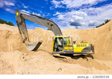 Heavy Excavator Digging Sand at Construction Site Under Blue Sky 126090536