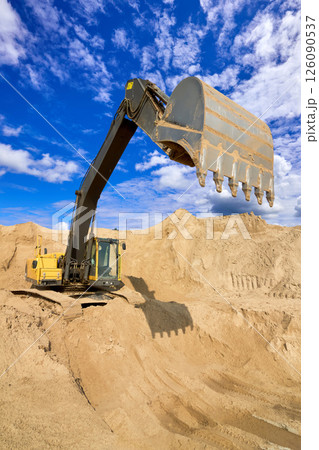 Heavy Excavator Digging Sand at Construction Site Under Blue Sky 126090537