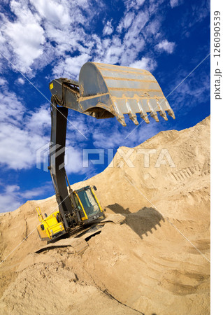 Heavy Excavator Digging Sand at Construction Site Under Blue Sky 126090539
