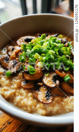 A warm bowl of oatmeal cooked in chicken broth, generously topped with fried mushrooms and fresh green onions, offering a healthy and savory meal 126091176