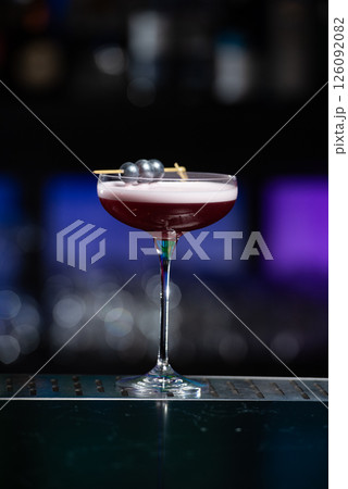purple cocktail with a foamy white top is garnished with skewered blueberries on a textured bar surface purple cocktail with a foamy white top is garnished with skewered blueberries on a textured bar surface 126092082