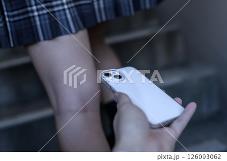 スカートを押さえながら階段を上る女子高生をスマホで盗撮する男性の手　 126093062