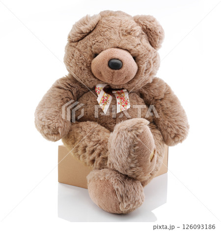 Big brown teddy bear sitting on a box with legs crossed 126093186