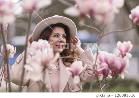 Woman magnolia flowers, surrounded by blossoming trees., hair down, white hat, wearing a light coat. Captured during spring, showcasing natural beauty and seasonal change. Woman magnolia flowers, surrounded by blossoming trees., hair down, white hat, wearing a light coat. Captured during spring, showcasing natural beauty and seasonal change. 126093310
