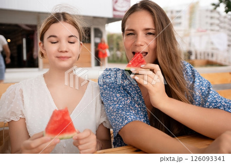 Watermelon Summer Festival Friends: Two women enjoy watermelon slices at outdoor summer festival cheerful, sunny day. Watermelon Summer Festival Friends: Two women enjoy watermelon slices at outdoor summer festival cheerful, sunny day. 126093341