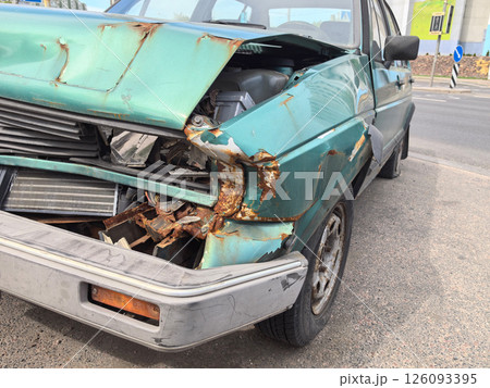 Old green car with severe damage parked on the roadside 126093395