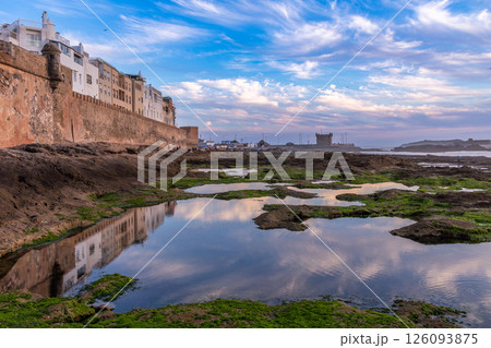 Moroccan town with reflection in low tide lakes at the walls of Skala de la Villa fortress bastion, Portuguese Mogador castle in evening time, Essaouira, Morocco 126093875