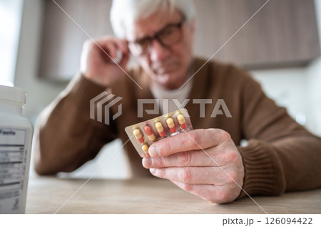 Pill blister check. Elderly man holds medication blister pack reading instructions with focused look Pill blister check. Elderly man holds medication blister pack reading instructions with focused look 126094422