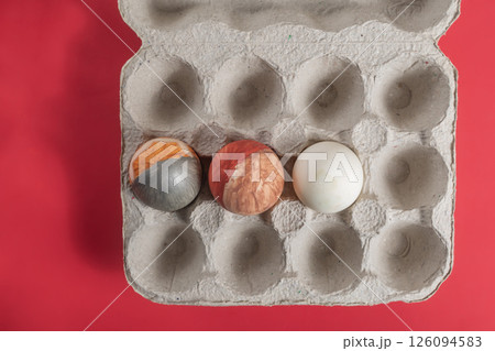 Decorated Easter eggs in a cardboard box on a vibrant red background for seasonal celebrations. Happy Easter 126094583
