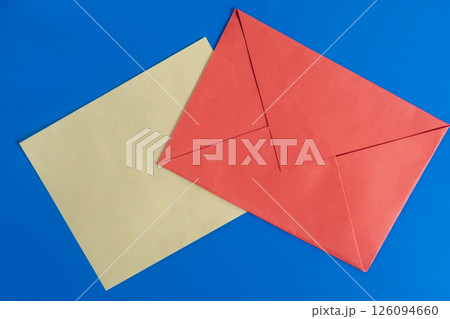 Bright red envelope with paper on a blue background surface. Bright red envelope with paper on a blue background surface. 126094660