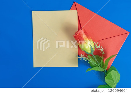 Red envelope with a blank card and a rose on a blue background. 126094664