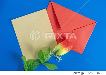 Red envelope with a blank card and an artificial flower on a blue background for Valentine's Day. 126094665