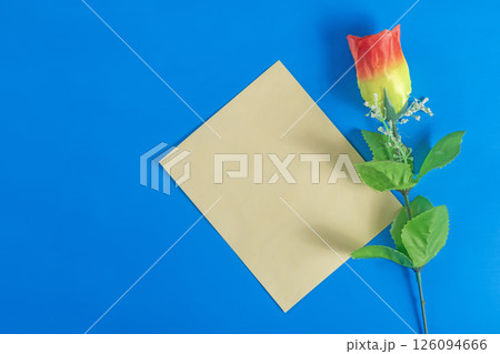 Colorful artificial rose flower and yellow paper blank card on dark blue background. 126094666