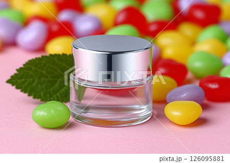 Small, clear cosmetic bottle with a silver cap sits on a pink surface, surrounded by colorful candies and accompanied by a vibrant green leaf, creating a playful and appealing presentation Small, clear cosmetic bottle with a silver cap sits on a pink surface, surrounded by colorful candies and accompanied by a vibrant green leaf, creating a playful and appealing presentation 126095881