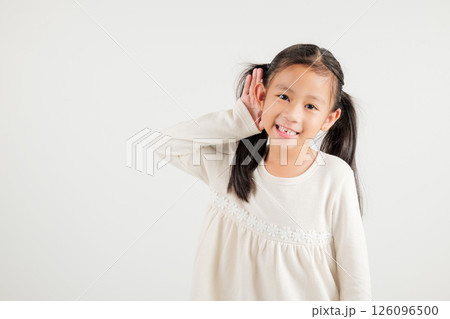 Portrait Asian young child smiling overhearing listening sound to gossip with attention with hand on ear studio shot isolated on white background with copy space hearing gesture, kindergarten kid girl 126096500