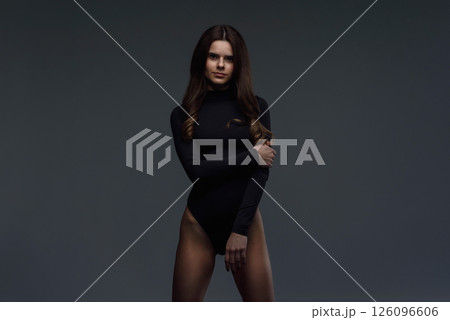 Beautiful slim brunette woman with perfect body in black bodysuit posing on dark gray background. Beautiful slim brunette woman with perfect body in black bodysuit posing on dark gray background. 126096606