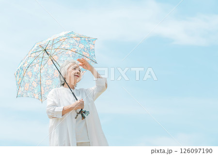 青空の下で日傘をさして散歩しているシニア女性 青空の下で日傘をさして散歩しているシニア女性 126097190