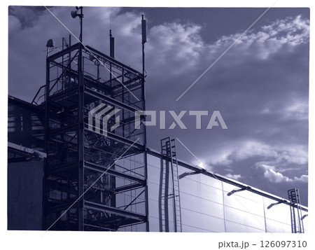 A communication tower under construction is seen against a backdrop of dark clouds. Scaffolding, antennas, and a sleek facade highlight the evolving structure. A communication tower under construction is seen against a backdrop of dark clouds. Scaffolding, antennas, and a sleek facade highlight the evolving structure. 126097310
