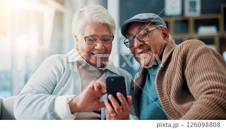 Senior couple, phone and laugh on couch in home with meme, mobile app and funny video on web in lounge. Elderly man, woman and relax with smartphone, joke and social media in retirement at apartment 126098808