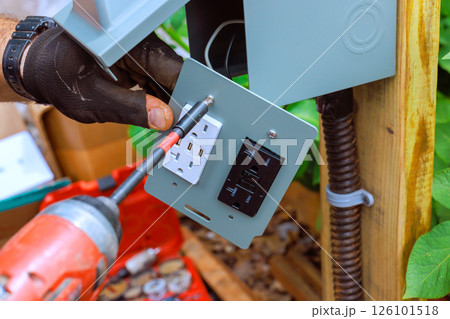 Electrician works on installing power outlet with USB ports in garden setting amid greenery. Electrician works on installing power outlet with USB ports in garden setting amid greenery. 126101518
