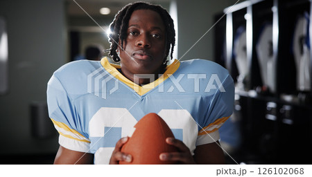 Black man, American football player and ball in portrait in locker room, strong and ready for sports contest. Person, athlete and equipment with confidence, career and club for competition in USA 126102068