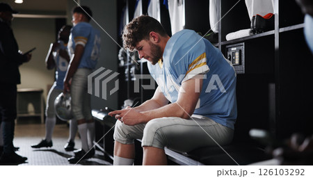 Football, player and athlete with phone in locker room for reading game plan, check notifications and match break. Sports, man and relax with smartphone for social media, online news and mobile chat 126103292