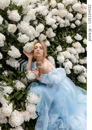 Woman in light blue ball gown poses near white lilacs Woman in light blue ball gown poses near white lilacs 126104082