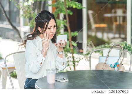 カフェでメイク直し・化粧・メイク・鏡を見る若い女性（保湿・UVカット・紫外線対策） 126107663