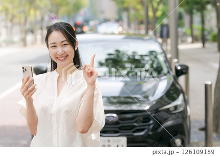 車の前でスマホを操作する若い女性 126109189