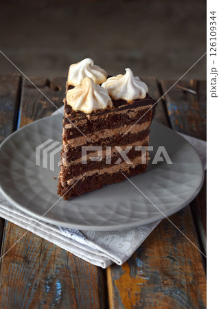 Piece of chocolate cake decorated with rosettes of meringue cream, chocolate-nut biscuit, caramel cream. Homemade baking Piece of chocolate cake decorated with rosettes of meringue cream, chocolate-nut biscuit, caramel cream. Homemade baking 126109344