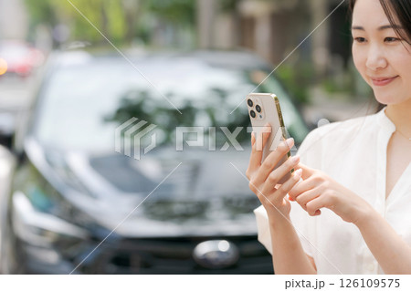 車の前でスマホを操作する若い女性 126109575