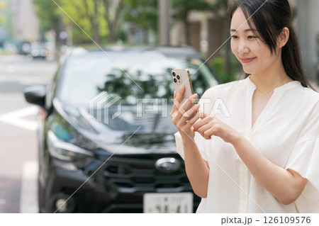 車の前でスマホを操作する若い女性 126109576